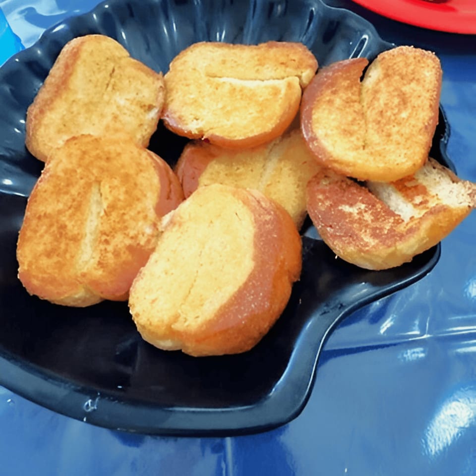 A black plate filled with several golden-brown, toasted bread slices on a blue surface.