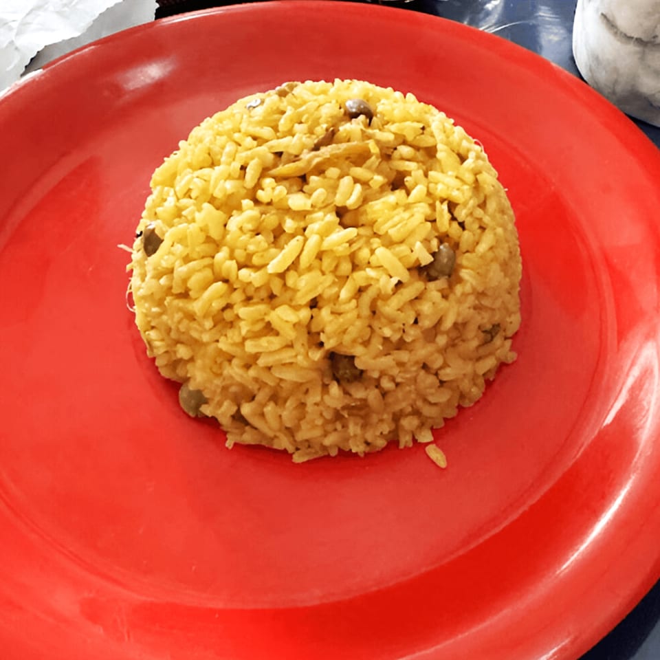 A mound of yellow Puerto Rican rice with pigeon peas on a bright red plate.
