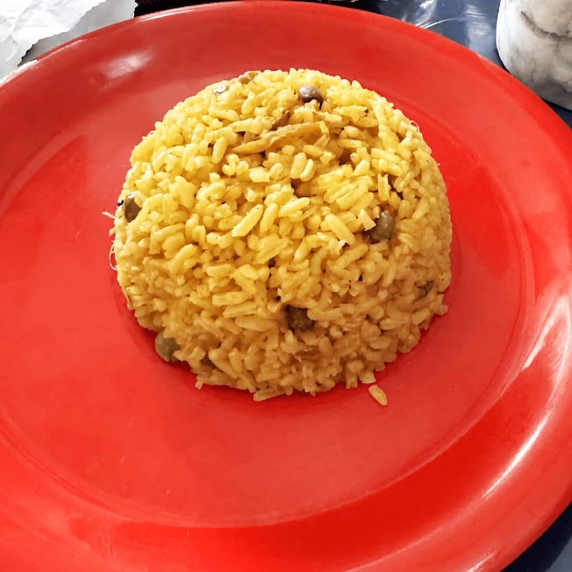 A mound of yellow Puerto Rican rice with pigeon peas on a bright red plate.