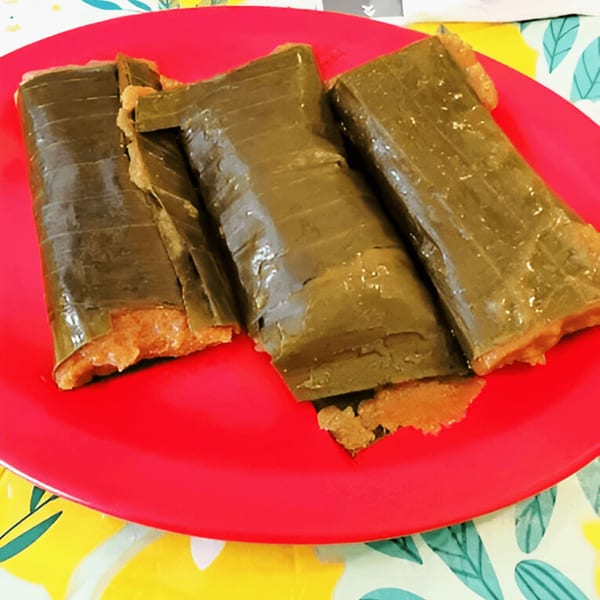 Three pasteles, a traditional Puerto Rican dish, wrapped in green banana leaves on a red plate.
