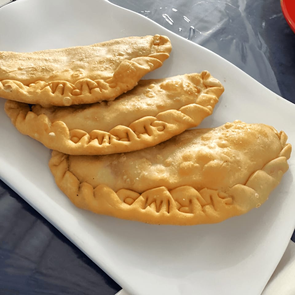 Three golden-brown Puerto Rican empanadillas with crimped edges on a white rectangular plate.