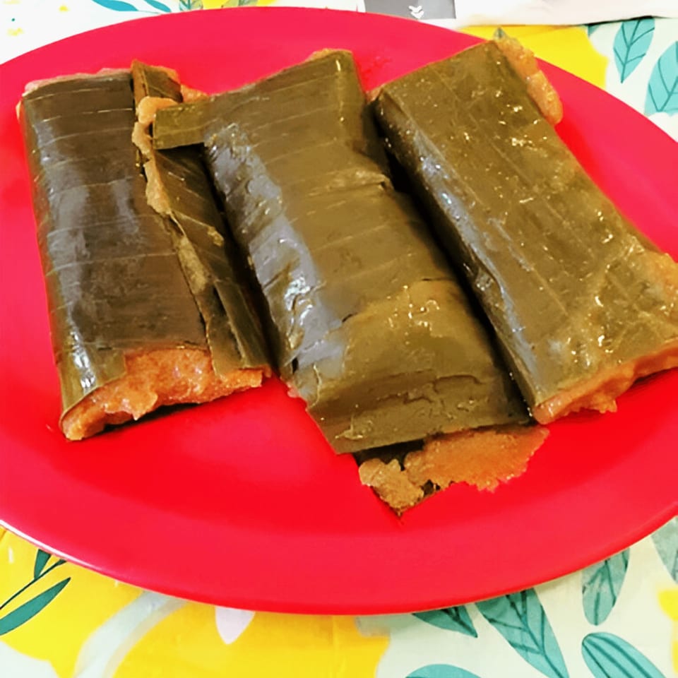 Three pasteles, a traditional Puerto Rican dish, wrapped in banana leaves on a red plate.