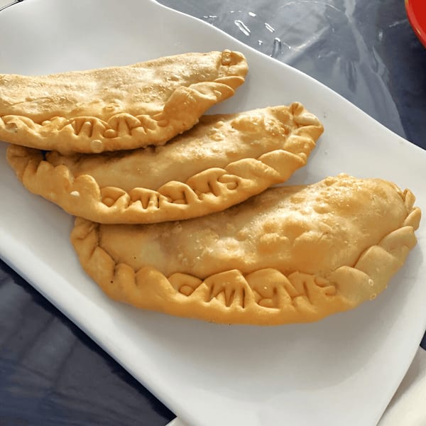 Three golden-brown Puerto Rican empanadillas with crimped edges, served on a white rectangular plate.